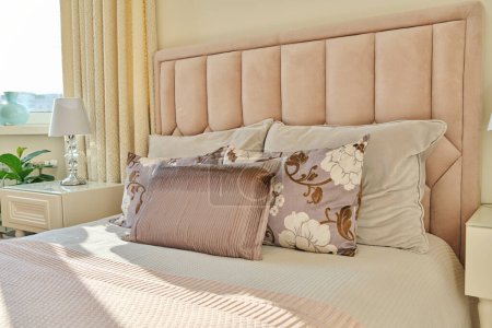 Foto de Dormitorio interior clásico de moda en colores marfil claro, en luz solar cálida, cama doble rosa con cojines de sofá, mesitas de noche con lámparas. Confort, hogar, estilo, decoración, concepto de diseño - Imagen libre de derechos