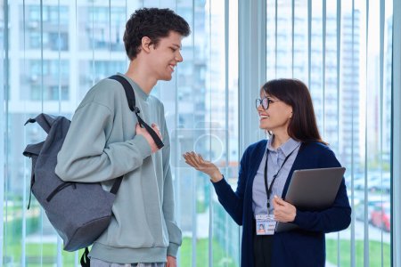 Photo for Meeting, conversation of female teacher and guy college student near window in hallway educational center. Talking woman educator pedagog tutor and young teenage male. Education, learning, studing - Royalty Free Image