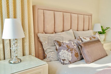 Photo for Classic trendy bedroom interior in light ivory colors, in warm sunlight, pink double bed with sofa cushions, bedside tables with lamps. Comfort, home, style, decor, design concept - Royalty Free Image