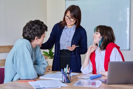 Photo for Middle aged female teacher giving lesson to teenage college students sitting at table. Education, knowledge, learning, studying, language courses, youth concept - Royalty Free Image