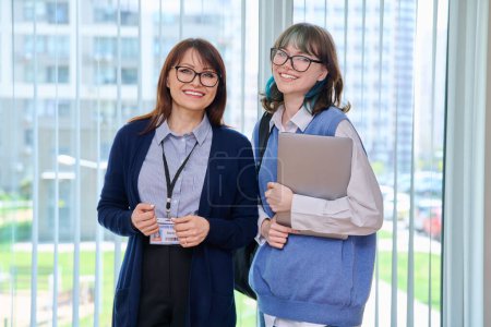 Photo for Portrait of middle aged female teacher and girl college student. Woman schoolmaster tutor and student looking at camera near window of hallway educational building. Education learning language courses - Royalty Free Image