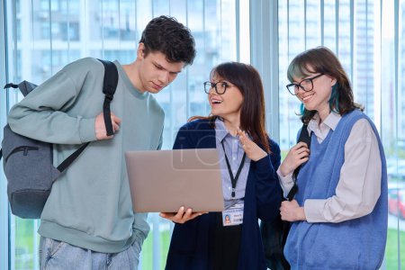 Photo for Female teacher, guy and girl, college students looking at laptop screen together standing near window in educational building. Education, knowledge, learning, language courses, youth concept - Royalty Free Image