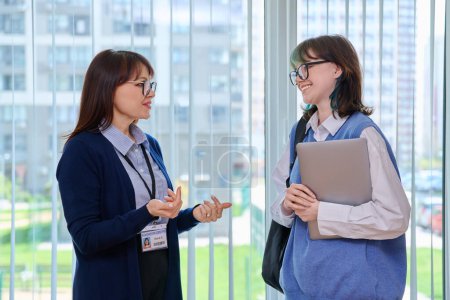 Photo for Meeting, conversation of female teacher and girl college student near window in hallway educational center. Talking woman educator pedagog tutor and young teenage female. Education, learning, studying - Royalty Free Image