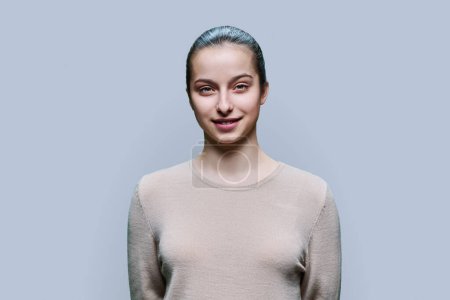 Téléchargez les photos : Portrait d'une adolescente de 15, 16 ans souriante regardant la caméra sur fond de studio gris. Adolescence, santé, éducation, loisirs, concept de style de vie - en image libre de droit