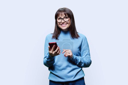 Joyful middle aged woman with phone on white studio background. Happy mature female looking at camera, lifestyle, good news emotions, 40s people concept