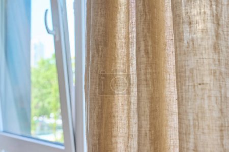Foto de Cortinas naturales de lino gris en la ventana, primer plano. Decoración de ventana textil, moda, estilo, concepto de diseño - Imagen libre de derechos