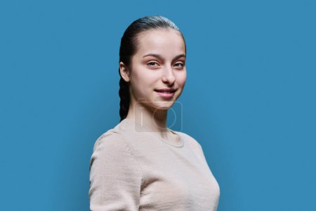 Téléchargez les photos : Portrait d'une adolescente de 15, 16 ans souriante regardant la caméra sur fond de studio bleu. Adolescence, santé, éducation, loisirs, concept de style de vie - en image libre de droit