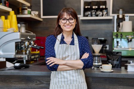 Photo for Portrait of confident mature female small business owner in apron near coffee shop counter. Smiling successful middle aged female with crossed arms. Food service occupation, staff, job, work concept - Royalty Free Image