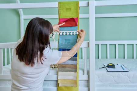 Foto de Mujer diseñadora eligiendo telas y accesorios textiles para decorar la habitación de los niños, una cortina decorativa para cama de bebé y cortinas en las ventanas. Servicios de diseño de sastrería colgante de productos textiles - Imagen libre de derechos