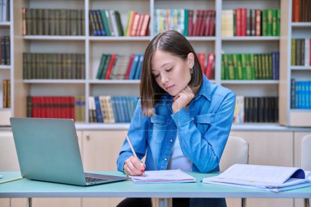 Photo for Young female university student studying inside library, using computer laptop, writing in notebook. Knowledge, education, youth, college university concept - Royalty Free Image