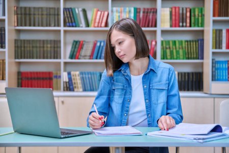 Photo for Young female university student studying inside library, using computer laptop, writing in notebook. Knowledge, education, youth, college university concept - Royalty Free Image