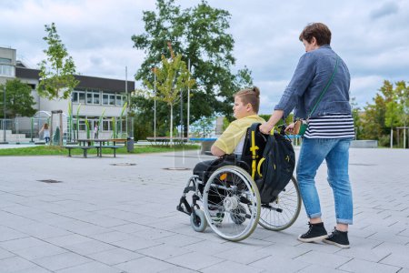Photo for Back view of woman with boy in wheelchair near the school building, copy space. Children, disability, education, activity, health, lifestyle concept - Royalty Free Image
