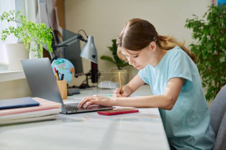Photo for Preteen girl studying at home at her desk using a laptop computer. High school, adolescence, education, technology, knowledge concept - Royalty Free Image