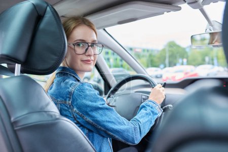 Photo for Teenage girl driver in glasses sitting behind wheel of car, smiling looking at camera, young female got license to drive car. Youth, auto school, lifestyle concept - Royalty Free Image