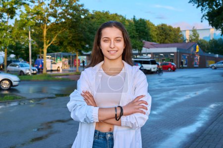 Photo for Portrait of confident smiling teenage girl looking at camera, with crossed arms outdoor, on town street in sunset light. Adolescence, urban lifestyle, young people concept - Royalty Free Image