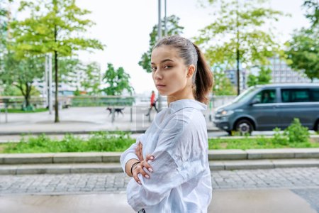 Photo for Portrait of serious confident teenage girl looking at camera, with crossed arms on street of modern city. Adolescence, urban lifestyle, young people concept - Royalty Free Image