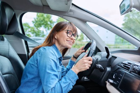 Téléchargez les photos : Femme d'âge moyen conducteur portant des lunettes assis derrière le volant dans la voiture. Transport, mode de vie, conduite, achat assurance réparation entretien de voiture, concept de personnes matures - en image libre de droit