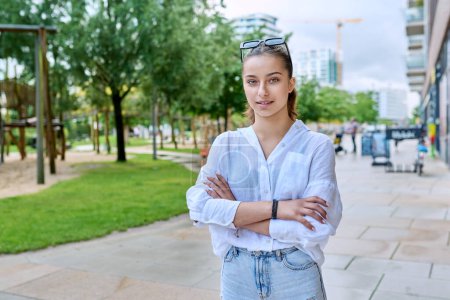 Photo for Portrait of confident smiling teenage girl looking at camera, with crossed arms on street of modern city. Adolescence, urban lifestyle, young people concept - Royalty Free Image