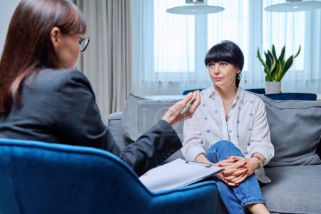 Mature 50s woman having therapy session with psychologist sitting on sofa in office. Mental health of senior people, counseling, treatment, psychological help support, psychology psychotherapy concept
