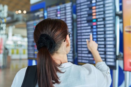 Téléchargez les photos : Passagère regardant l'horaire des vols à l'aéroport. Une femme vérifie l'heure de décollage. Transport aviation de passagers, tourisme, voyages, concept de personnes - en image libre de droit