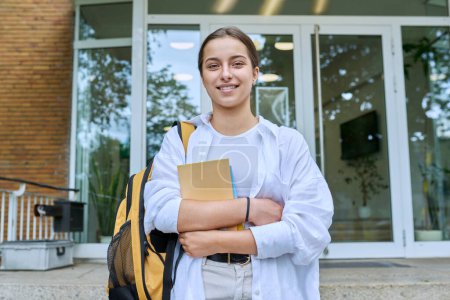 Téléchargez les photos : Portrait d'élève du secondaire, fille souriante avec sac à dos regardant la caméra, en plein air sur les marches du bâtiment éducatif. Adolescence, 15, 16, 17 ans, style de vie, concept éducatif - en image libre de droit