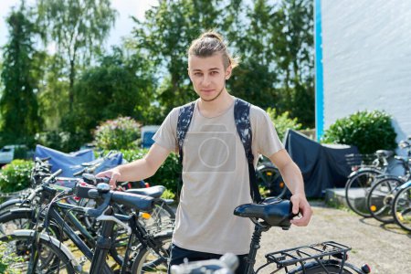 Téléchargez les photos : Étudiant adolescent avec sac à dos avec vélo de plein air, fond de bâtiment éducatif, parking à vélo. Jeunesse, transport, mode de vie des étudiants concept - en image libre de droit