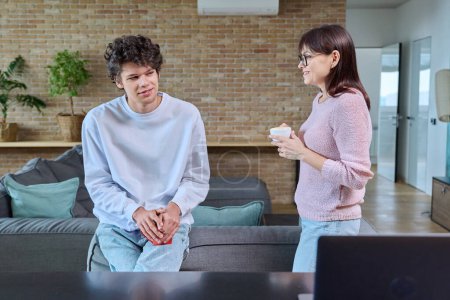Photo for Middle aged mother and son 19, 20 years old talking together at home in living room. Family, relationships, communication mom teenage son, people concept - Royalty Free Image