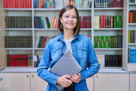 Photo for Portrait of smiling young female university student looking at camera, standing posing with laptop in library classroom of educational building. Knowledge, higher education, youth concept - Royalty Free Image