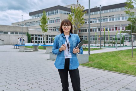 Photo for Middle-aged confident woman school teacher, mentor, pedagogue, psychologist, counselor, social worker with digital tablet in hands posing near school building, outdoor. Education, teaching, school - Royalty Free Image