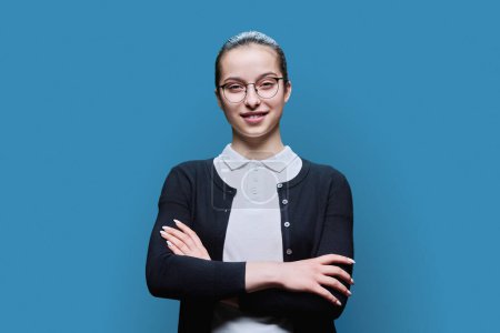 Photo for Portrait confident smiling teenager girl with glasses on blue background. Positive female 16, 17 years old looking at camera with crossed arms high school student lifestyle adolescence youth - Royalty Free Image