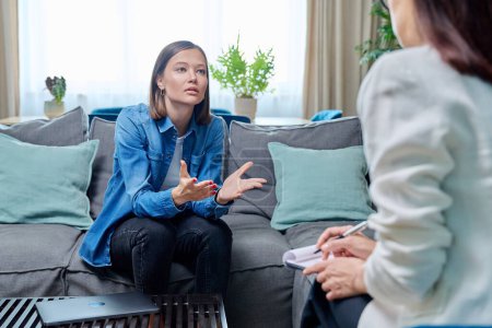 Photo for Sad young woman at therapy session with psychologist, psychiatrist. Therapist counselor and unhappy female patient on sofa in office. Psychology counseling treatment psychotherapy mental health youth - Royalty Free Image