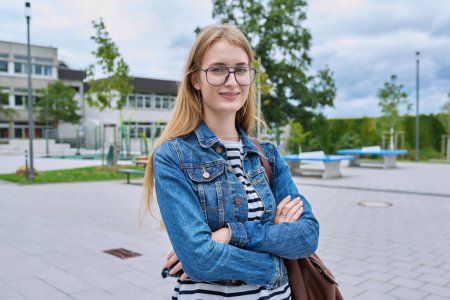Photo for Portrait of confident teenage high school student girl with backpack, outdoor. Smiling teen schoolgirl looking at camera with crossed arms, school building background. Adolescence education knowledge - Royalty Free Image