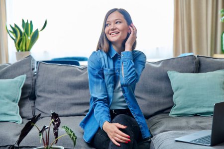 Foto de Retrato de una joven mujer atractiva sonriente mirando a la cámara, sentada en el sofá en la sala de estar en casa. Estilo de vida, ocio, concepto de juventud - Imagen libre de derechos