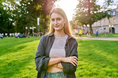 Photo for Portrait of young teenage smiling female looking at camera outdoor. Confident friendly cool girl with crossed arms in sunny sunset light. Youth, lifestyle education concept - Royalty Free Image