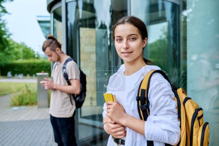 Téléchargez les photos : Portrait de lycéen, fille souriante avec sac à dos regardant la caméra, extérieur, fond de bâtiment éducatif. Adolescence, 15, 16, 17 ans, style de vie, concept éducatif - en image libre de droit