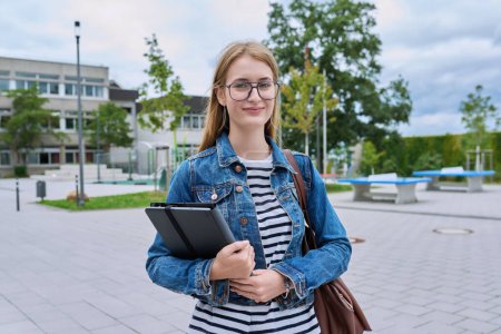 Photo for Portrait of teenage girl high school student, smiling female in glasses with backpack holding digital tablet, outdoor near educational building. Adolescence, education, knowledge concept - Royalty Free Image