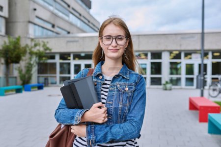 Foto de Retrato de estudiante de secundaria adolescente, mujer sonriente en gafas con mochila sosteniendo tableta digital, al aire libre cerca del edificio educativo. Adolescencia, educación, concepto de conocimiento - Imagen libre de derechos