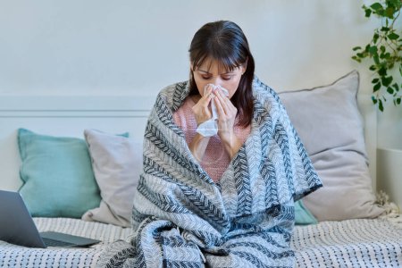 Photo for Sick mature woman with blanket sneezing and coughing into napkin. Seasonal colds, season flu colds, health people concept - Royalty Free Image