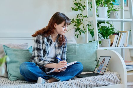 Photo for Girl college student watching educational webinar, sitting on couch at home with laptop taking notes in notebook. Education, training, technology, youth concept - Royalty Free Image
