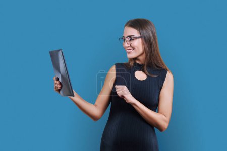 Foto de Joven mujer de negocios con tableta digital sobre fondo de estudio azul. Elegante mujer de moda en vestido negro mirando la pantalla del gadget. Tecnologías, negocios, trabajo, trabajo, ejecutivo, ocupación - Imagen libre de derechos