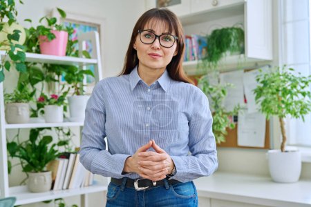 Photo for Portrait of confident smiling middle-aged woman in glasses, casual clothes with folded hands, looking at camera in home interior. 40s age, lifestyle, health, mature lady concept - Royalty Free Image