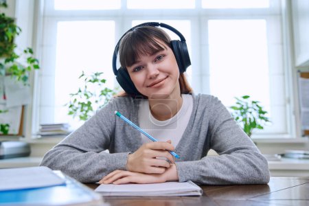 Photo for Web camera view of teenage student girl in headphones looking at camera sitting at desk with textbooks notebooks. Online lesson video chat call conference. Technology education training e-learning - Royalty Free Image