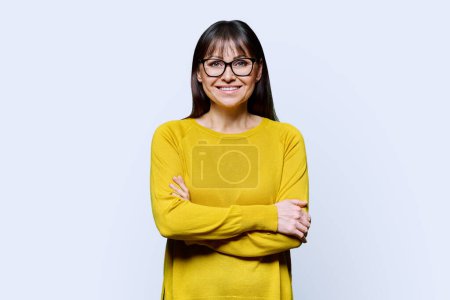 Téléchargez les photos : Portrait de femme confiante mature souriante sur fond de studio blanc. Femme d'âge moyen en jaune, lunettes regardant la caméra, mode de vie, santé, travail, concept de personnes 40s - en image libre de droit