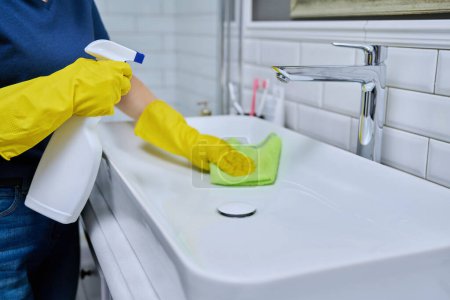 Foto de Primer plano del fregadero de limpieza con grifo en el baño, manos femeninas en guantes protectores de goma con detergente de limpieza y trapo profesional. Limpieza de la casa limpieza limpieza concepto de servicio de limpieza - Imagen libre de derechos