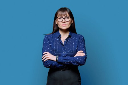 Photo for Portrait of serious confident business mature woman with crossed arms on blue studio background. Successful attractive middle-aged female looking at camera. Business, work, job, lifestyle, 40s people - Royalty Free Image