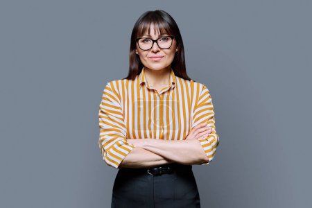 Photo for Portrait of confident smiling middle aged business woman with crossed arms on grey background. Positive female with glasses looking at camera. 40s professional, beauty health lifestyle work services - Royalty Free Image