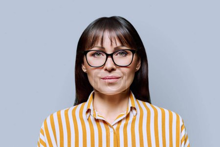 Photo for Portrait of serious middle aged woman on grey background. Confident female with glasses looking at camera. 40s professional, beauty health lifestyle work business services - Royalty Free Image
