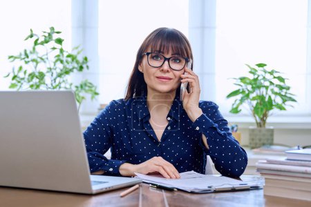Photo for Portrait of mature woman working at home on computer laptop. Smiling middle-aged female wearing glasses looking at camera while sitting at desk in home office. Remote business teaching work, freelance - Royalty Free Image