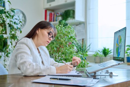 Photo for Mature serious business woman working at a computer, workplace financier leader boss entrepreneur. Focused middle-aged female looking at a laptop screen with graphs and diagrams, marketing management - Royalty Free Image