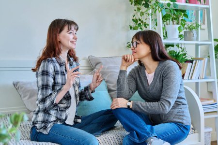 Photo for Talking happy smiling mother and teenage daughter sitting together on couch at home. Family, communication, motherhood, friendship, relationship between parent and daughter 18-20 years old - Royalty Free Image